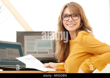 Succès smiling mature businesswoman using laptop et l'ordinateur tout en faisant quelques formalités administratives au bureau. Banque D'Images