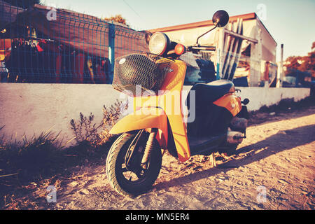 Scooter jaune garée sur une route du sol dans un après-midi ensoleillé Banque D'Images