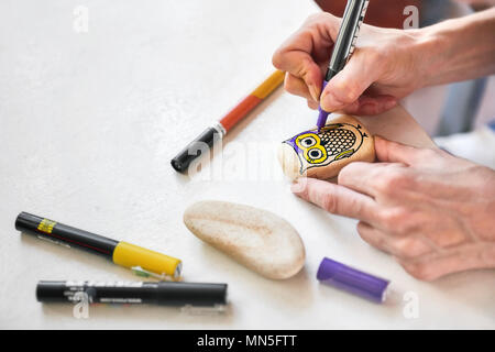 Caucasian woman painting un hibou sur une pierre. La peinture de Pierre passe-temps, les arts et métiers. Banque D'Images