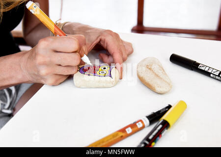 Caucasian woman painting un hibou sur une pierre. La peinture de Pierre passe-temps, les arts et métiers. Banque D'Images