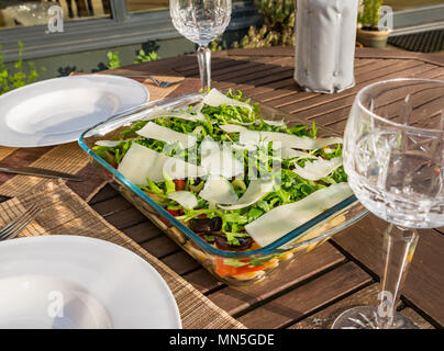 Table extérieure sous le soleil avec de la salade de pâtes plats, verres à vin en cristal et une bouteille de vin blanc frais dans le refroidisseur Banque D'Images