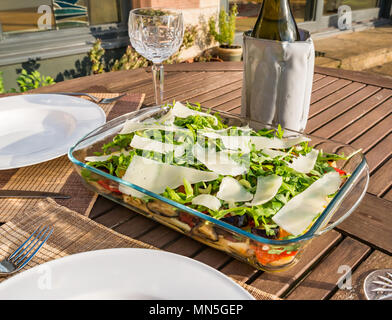 Table extérieure sous le soleil avec de la salade de pâtes plats, verres à vin en cristal et une bouteille de vin blanc frais dans le refroidisseur Banque D'Images