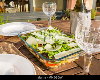 Table extérieure sous le soleil avec de la salade de pâtes plats, verres à vin en cristal et une bouteille de vin blanc frais dans le refroidisseur Banque D'Images