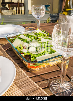 Table extérieure sous le soleil avec de la salade de pâtes plats, verres à vin en cristal et une bouteille de vin blanc frais dans le refroidisseur Banque D'Images