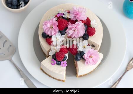 Une tranche de gâteau au fromage vegan fait maison pour le dessert. Décoré avec des framboises, bleuets et fleurs fraîches. Banque D'Images