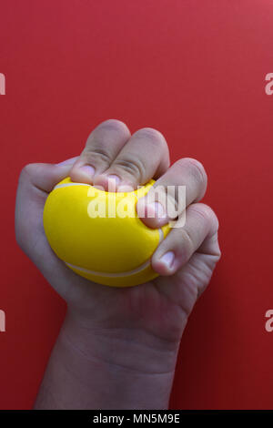 Woman squeezing une balle anti-stress, close-up, sur un fond rouge avec l'exemplaire de l'espace. Banque D'Images