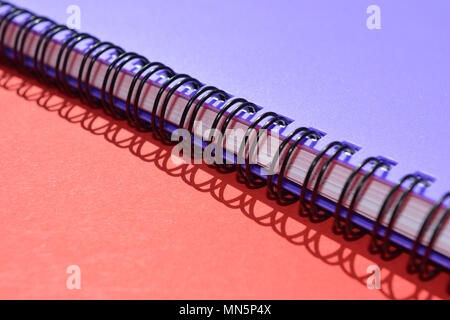 Un circuit fermé, violet, relié en spirale portable sur un fond rouge avec l'ombre de la spirale Banque D'Images