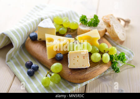 Snack-fromage avec plusieurs sortes, servi avec du pain et des raisins sur une planche à découper en bois Banque D'Images