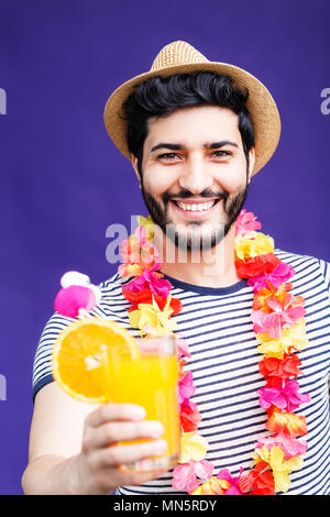 Homme barbu habillé en lei sur le cou et le chapeau et est titulaire d'boisson à l'orange sur fond violet, vacances concept, studio shot isolé Banque D'Images