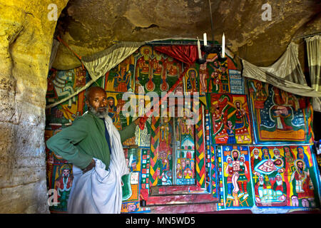 Prêtre montre peintures sur toile avec les thèmes bibliques dans l'interieur de l'église rupestres Mikael, Mellehayzengi Tsaeda Amba, Tigray, Éthiopie Banque D'Images