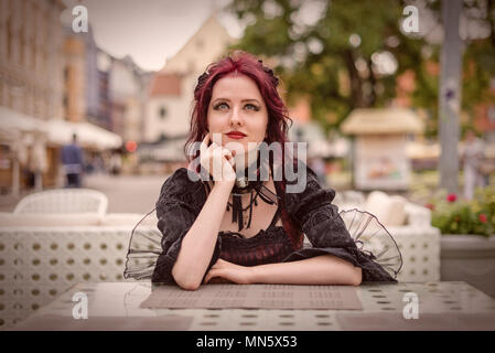 Superbe jeune femme rousse assise dans un café en plein air habillé en mode rétro vêtements. Banque D'Images