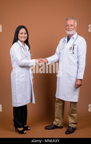 Multi-ethnic couple mature médecins contre fond brun Banque D'Images