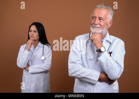 Multi-ethnic couple mature médecins contre fond brun Banque D'Images