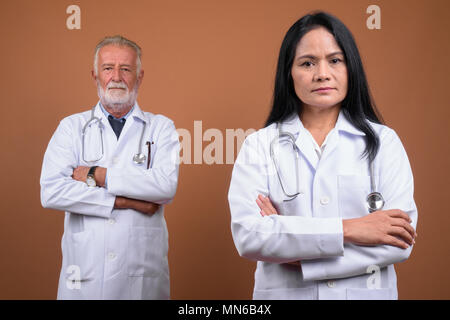 Multi-ethnic couple mature médecins contre fond brun Banque D'Images