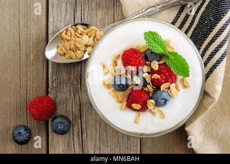 Yaourt à la grecque avec les framboises, bleuets et granola, les frais généraux sur scène en bois rustique Banque D'Images