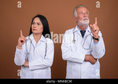 Multi-ethnic couple mature médecins contre fond brun Banque D'Images