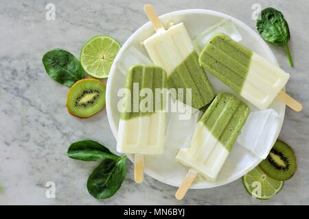 Sucettes glacées smoothie vert sain avec kiwi, citron vert et les épinards sur une plaque en marbre blanc, overhead view Banque D'Images