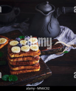Pile de tranches de pain frit carrés avec du chocolat et des tranches de banane sur une planche de bois brun, du pain perdu pour le petit déjeuner Banque D'Images