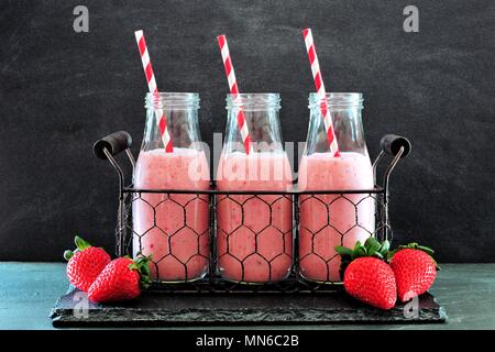 Les smoothies fraises dans des bouteilles avec des pailles dans un panier métallique contre un arrière-plan en ardoise foncé Banque D'Images