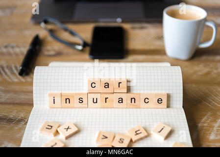 Gros plan sur ordinateur portable sur la table de bois, l'arrière-plan l'accent sur des pièces en bois avec des lettres formant des mots d'assurance voiture. Concept d'image. Banque D'Images