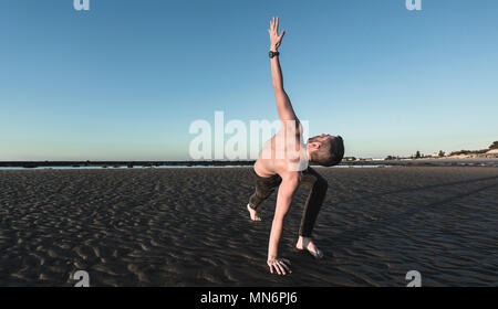 Jeune homme faisant du yoga sur la plage de sable de Sanlucar de Barrameda quand la marée est basse Banque D'Images