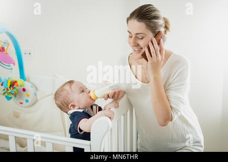 Portrait of smiling young man par téléphone et nourrir son petit fils bébé Banque D'Images