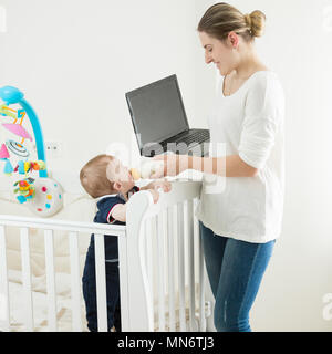 Portrait de jeunes travailleurs emploed woman working on laptop tout en alimentant son bébé avec le lait de la bouteille Banque D'Images