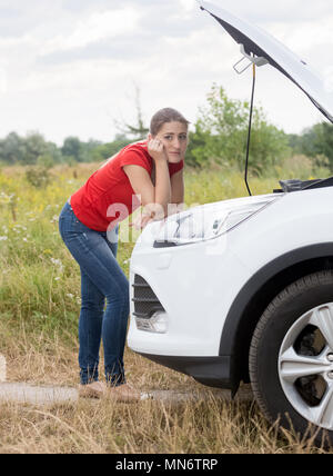 Contrarié young woman leaning on voiture cassée dans le champ à la caméra en Banque D'Images