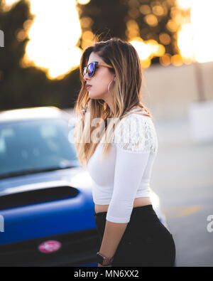 Jeune belle latina avec des lunettes pour le coucher du soleil avec sa voiture Banque D'Images