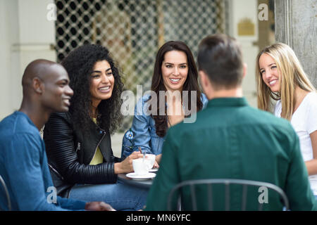 Groupe multiracial de cinq amis en buvant un café ensemble. Trois femmes et deux hommes au café, parler, rire et profiter de leur temps. Les concepts de vie et de l'amitié avec des personnes réelles maquettes Banque D'Images