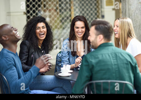 Groupe multiracial de cinq amis en buvant un café ensemble. Trois femmes et deux hommes au café, parler, rire et profiter de leur temps. Les concepts de vie et de l'amitié avec des personnes réelles maquettes Banque D'Images