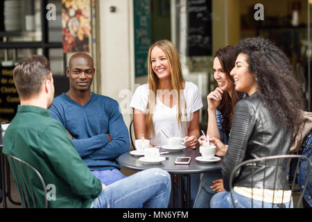 Groupe multiracial de cinq amis en buvant un café ensemble. Trois femmes et deux hommes au café, parler, rire et profiter de leur temps. Les concepts de vie et de l'amitié avec des personnes réelles maquettes Banque D'Images