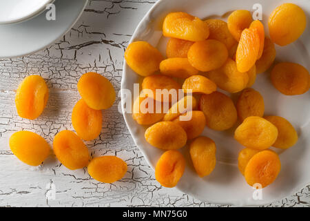 Fruits abricots secs entiers sur plaque blanche sur fond de table en bois blanc rustique d'en haut Banque D'Images