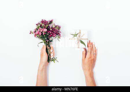 Woman's hands holding petit bouquet et petite boîte-cadeau attaché avec de la corde de jute. Télévision jeter la composition avec fleurs roses et présent sur fond blanc. Banque D'Images