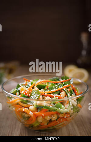 Salade de nouilles thaïlandaise de carottes et de concombre avec les pois chiches, la coriandre et les graines de sésame dans une sauce aigre-douce en verrerie sur une table en bois. Le conce Banque D'Images