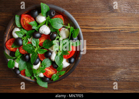 Salade italienne classique avec de la mozzarella, tomates, basilic, olives et huile d'olive. Caprese dans une cuvette d'argile sur un fond de bois. Vue de dessus, copiez l'espace. Banque D'Images