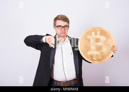 Malheureux homme tenant un bitcoin or et montrant vers le bas. Banque D'Images