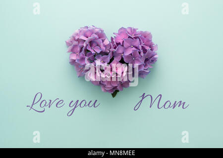 T'aime Maman Texte & forme de coeur fait de fleurs violettes sur fond bleu. Happy Mother's Day carte de vœux. Mise à plat. Banque D'Images