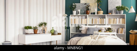 Plateau en bois blanc avec tasse de thé et des biscuits et pot placé sur un lit king-size dans la chambre verte intérieur avec des plantes fraîches et bibliothèque Banque D'Images