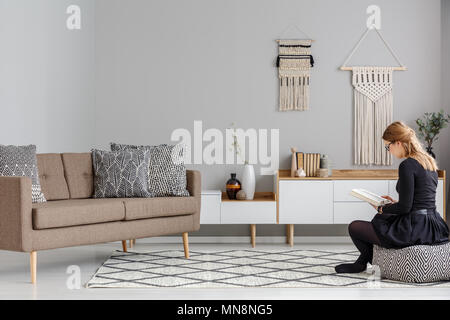 Femme sur pouf à motifs près de brown canapé dans salon moderne avec un décor intérieur DIY. Photo réelle Banque D'Images