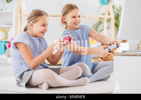 Deux jeunes filles à jouer à des jeux vidéo assis sur un tapis blanc à la bonne tenue et pads Banque D'Images