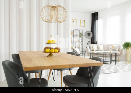 Salle à manger lumineuse intérieur avec des fruits sur la table en bois, des chaises et des tubes gris mur. Salle de séjour dans l'arrière-plan Banque D'Images