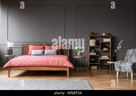 Fleurs sur table en bois à côté du lit de rose dans d'élégantes chambres avec intérieur gris fauteuil à motifs Banque D'Images