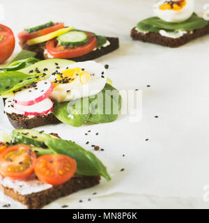 Des sandwichs d'été avec des légumes frais, oeufs, avocat, tomate, le pain de seigle sur table en marbre clair. Amuse-gueule pour partie. Close up. Banque D'Images