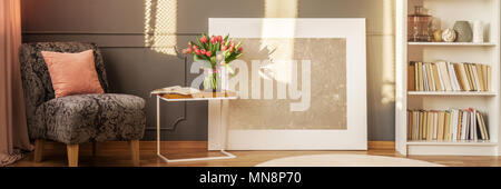 L'affiche moderne placé sur le plancher de salle de séjour avec l'intérieur gris fauteuil floral, des tulipes et des livres sur rack blanc Banque D'Images