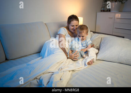 Mignon bébé garçon et jeune mère jouant avec de la peluche jouet avant d'aller dormir Banque D'Images