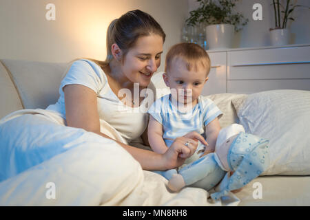 Portrait of smiling young woman giving peluche à son bébé avant d'aller dormir Banque D'Images