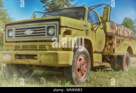 'Le jaune' un grand camion jaune rouille et abandonnés dans un champ d'herbe verte avec ciel bleu Banque D'Images