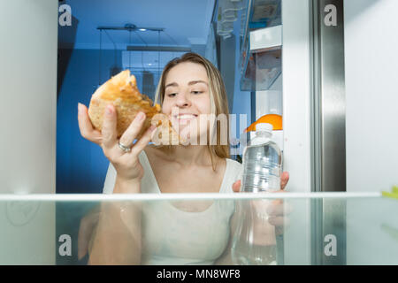 Portrait de jeune femme à la coupe faim nuit choix entre pizza riche en calories et une bouteille d'eau Banque D'Images