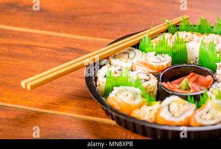 Close up d'un grand ensemble de délicieux rouleaux de sushi japonais sur une plaque en plastique noir sur une table en bois Banque D'Images